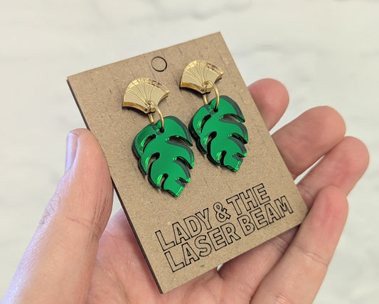 Art deco style fan top earrings with a green drop leaf on a cardboard backing card. 