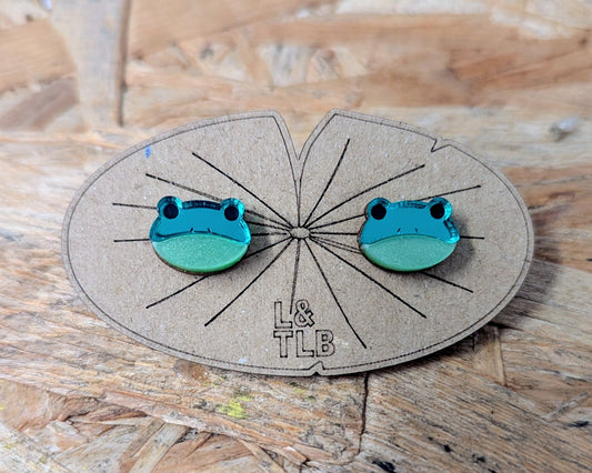Pair of green frog-shaped earrings on a branded lily pad shaped card with 'L&TLB' written on.